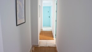 A hallway with a framed abstract artwork on the left, a blue door at the end, and a brown rug on the floor. - Hostal Salitre (Conil de la Frontera)