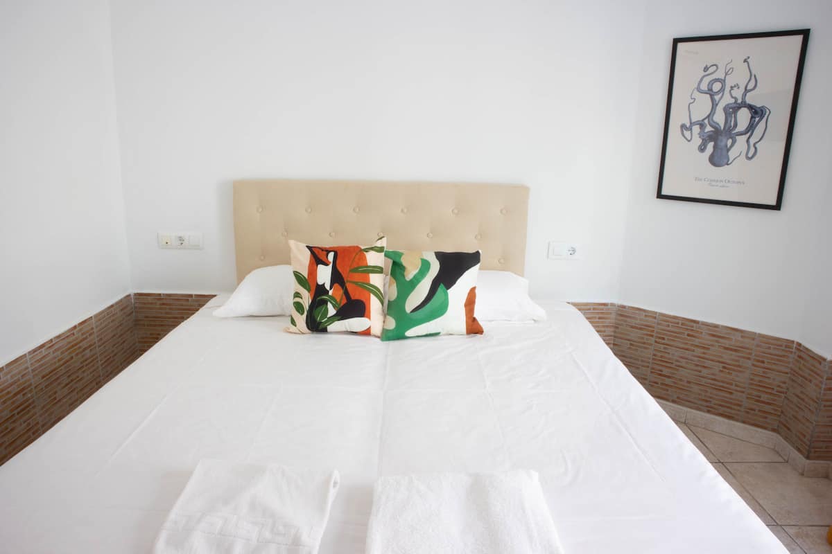 Una cama bien hecha con dosel acolchado, ropa de cama blanca y almohadas coloridas.
