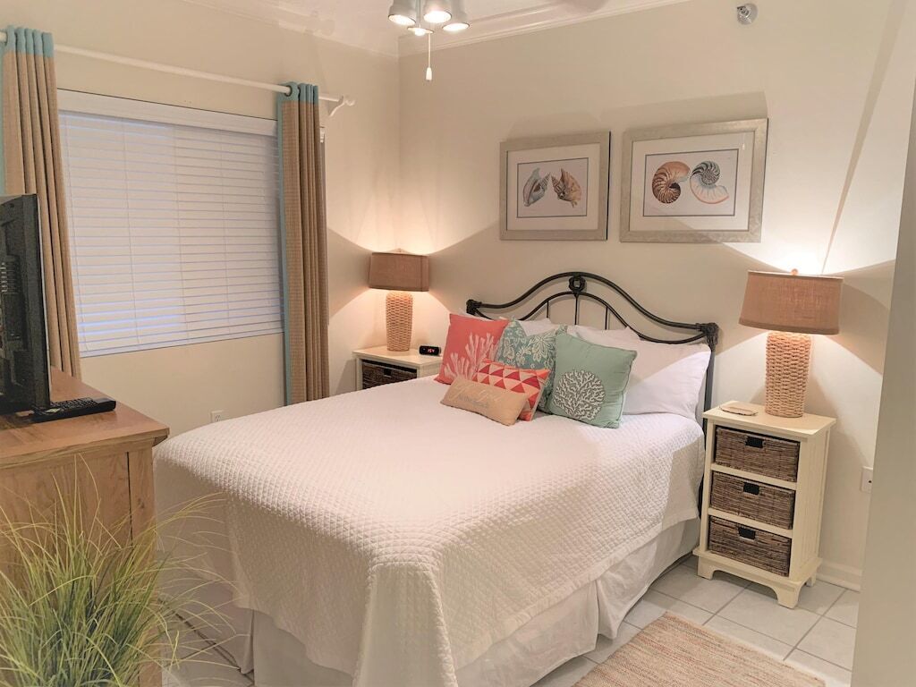 A bedroom with a bed, bedside lamps, a TV, and artwork on the wall.