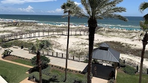 Blick auf einen Strand mit einer Holzpromenade, Palmen und einem kleinen Pavillon.