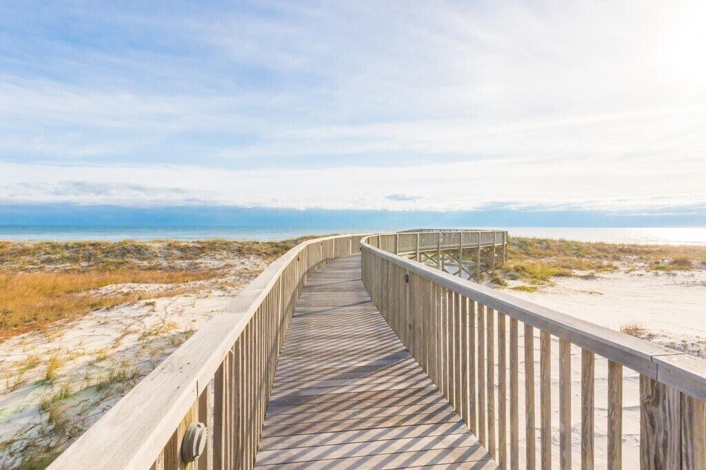 Ein hölzerner Steg führt zu einem Strand mit freiem Blick auf das Meer.