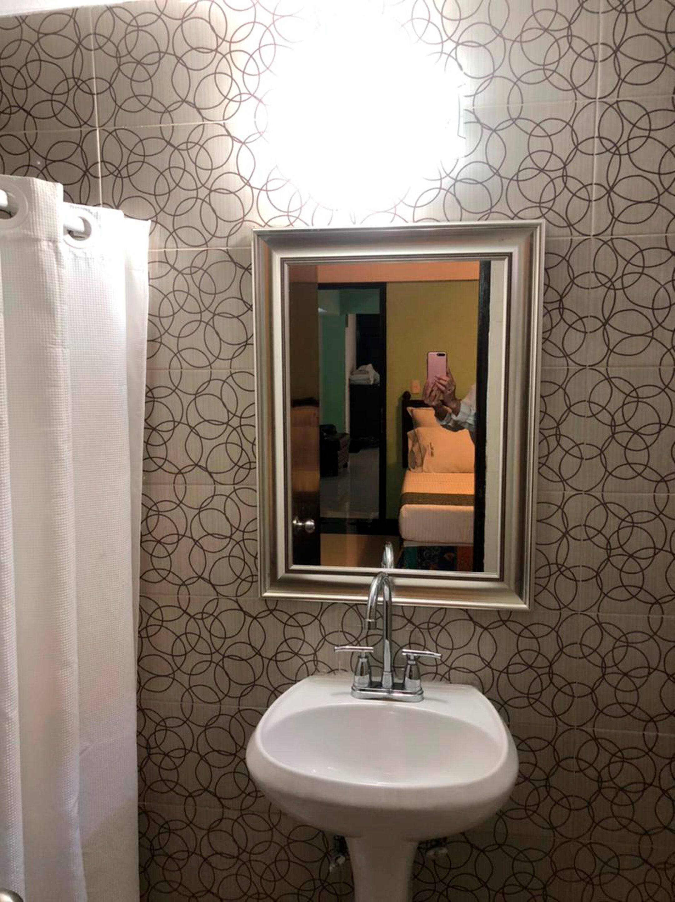 Un baño con un lavabo blanco, un espejo encima y papel tapiz estampado.