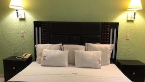 Habitación de hotel con una cama grande, varios almohadones, dos lámparas de noche, un teléfono en la mesita de noche y una colcha estampada.
