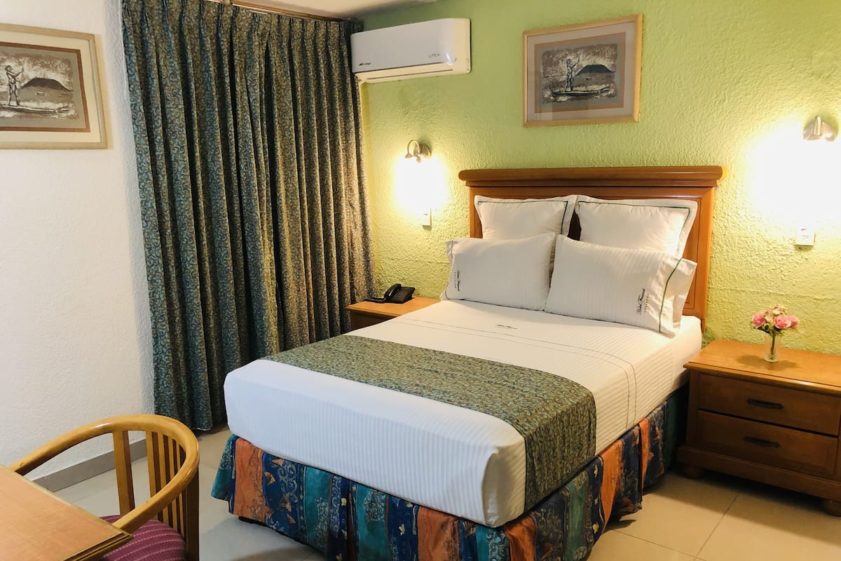 Habitación de hotel con cama, escritorio, silla, mesita de noche con teléfono y aire acondicionado de pared.