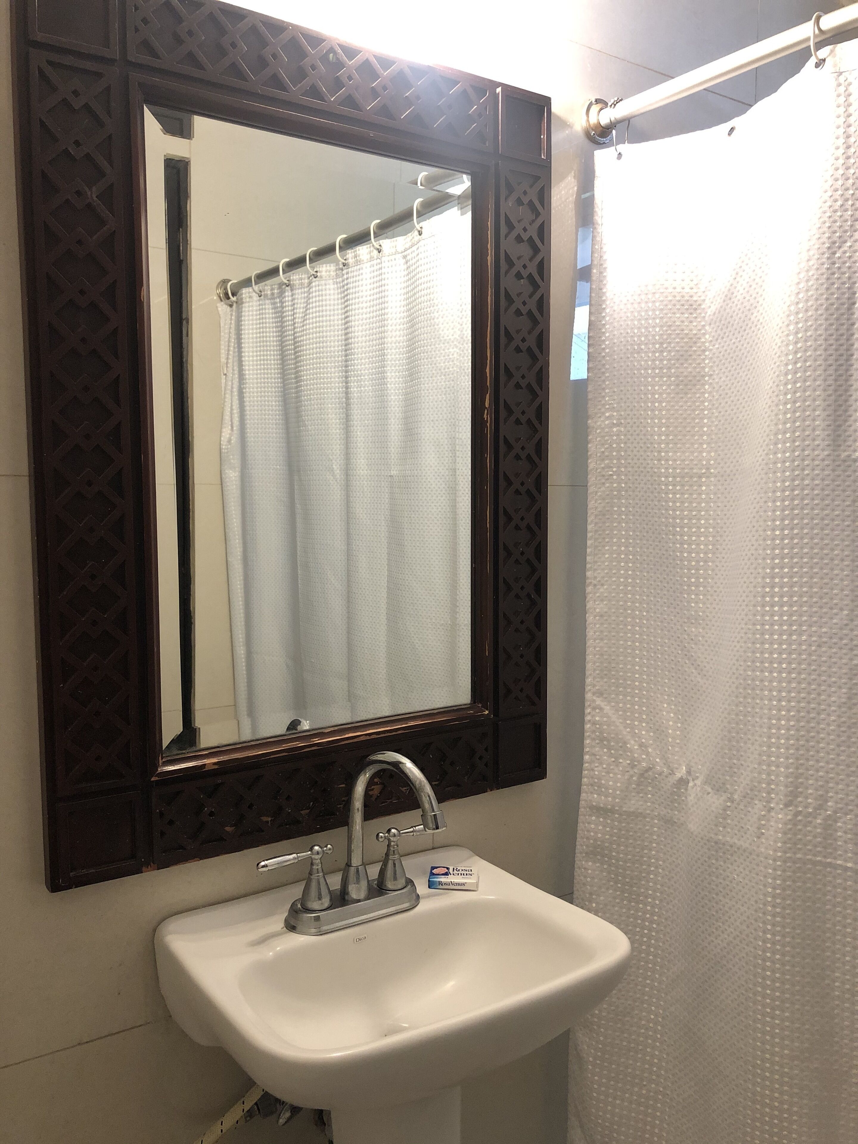A bathroom with a white sink, a mirror with a decorative frame, and a shower curtain.
