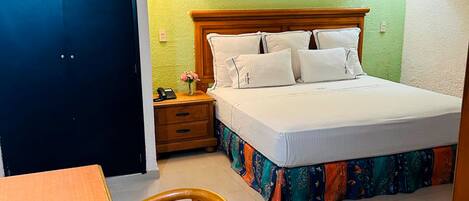 A hotel room with a bed, bedside table, lamp, chair, and a painting on the wall.