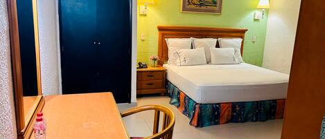 Habitación de hotel con cama, escritorio, silla, mesita de noche y un cuadro en la pared.