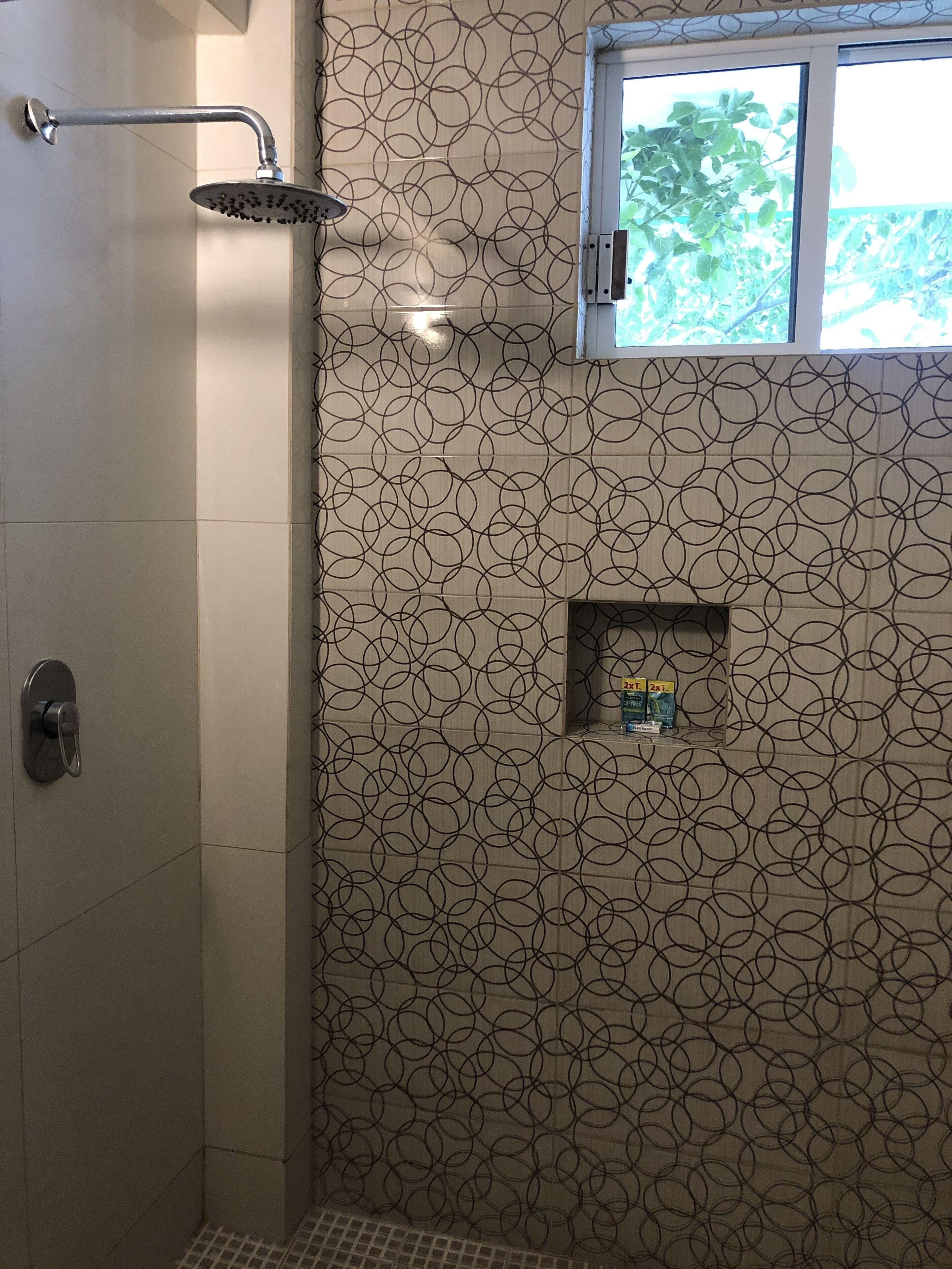 A bathroom with a shower, a window, and a patterned wall.