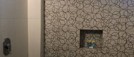 A bathroom with a shower, a window, and a patterned wall.