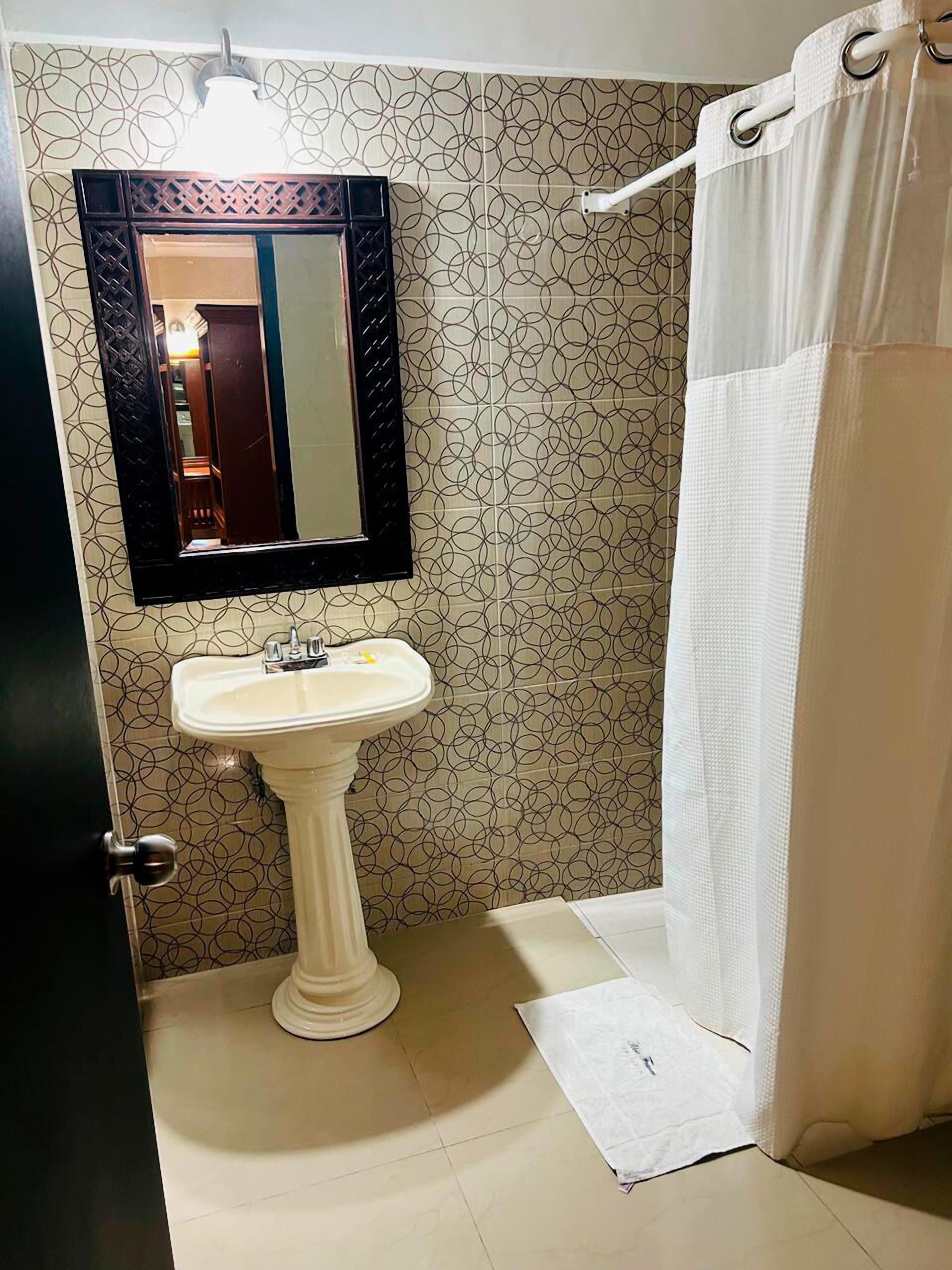 A bathroom with a pedestal sink, a mirror with a black frame, and a shower curtain.