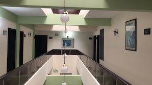 Un pasillo de hotel con una escalera central, paredes verdes y puertas numeradas.