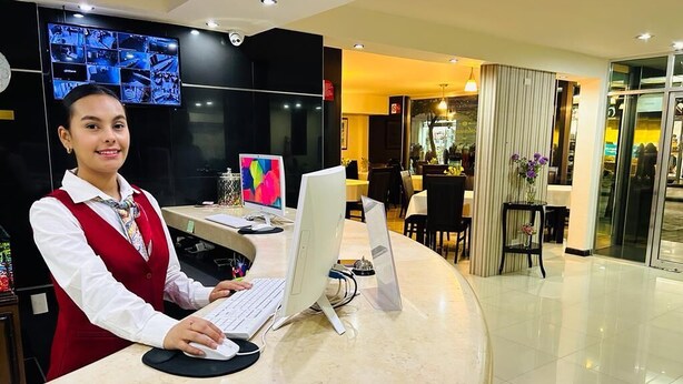 Mostrador de recepción de hotel con una computadora, una pantalla digital y vista del área de recepción.
