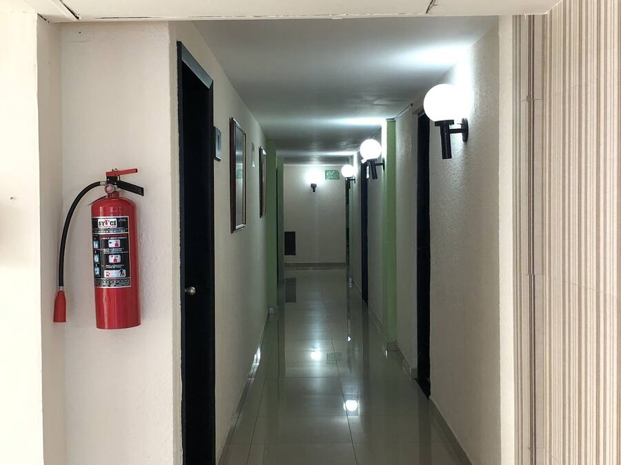 A hallway with a fire extinguisher, a ceiling-mounted air conditioning unit, and wall-mounted lights.