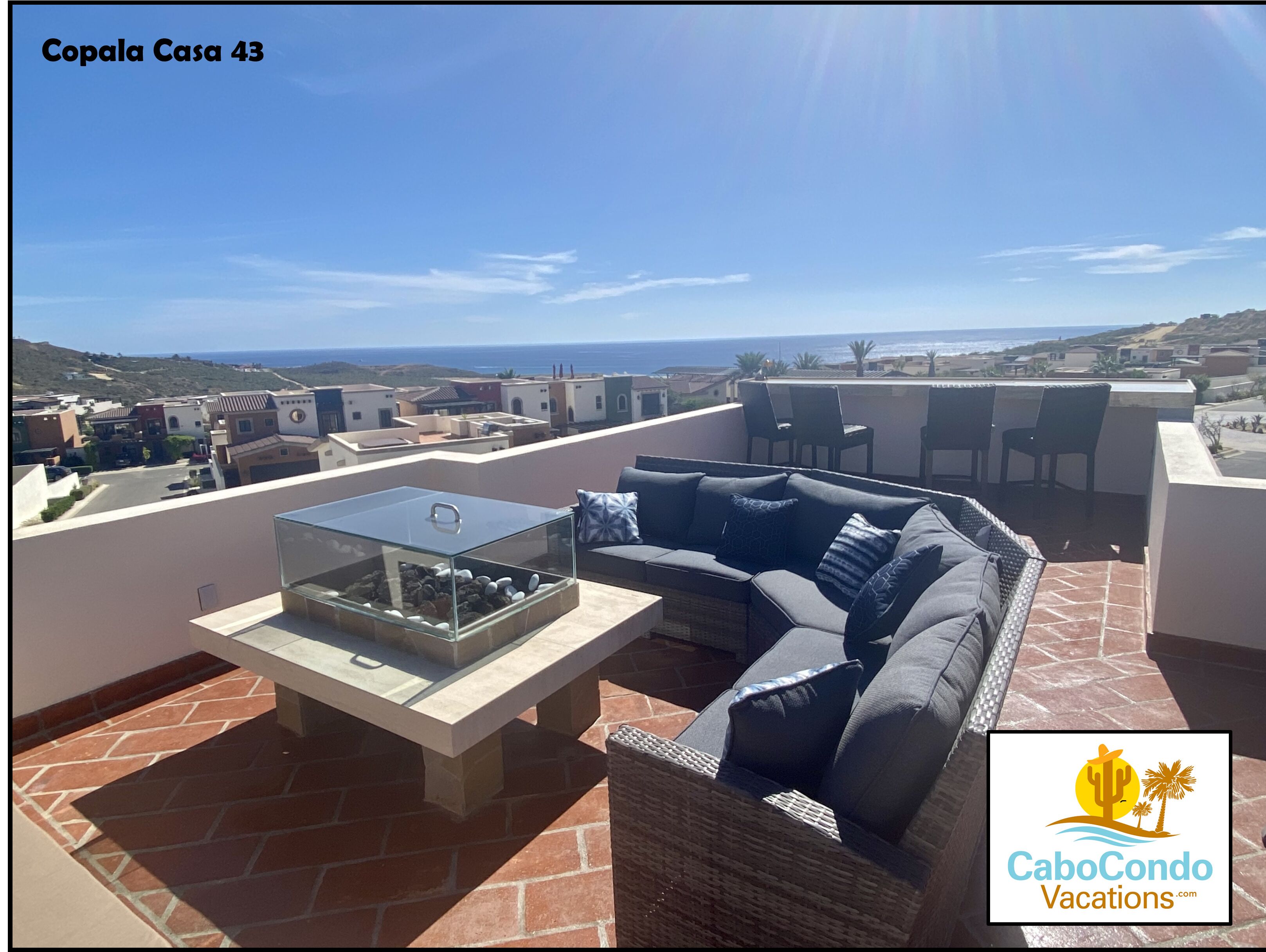 Une terrasse sur le toit avec une table à plateau de verre, un canapé gris et une vue sur la mer et les collines.