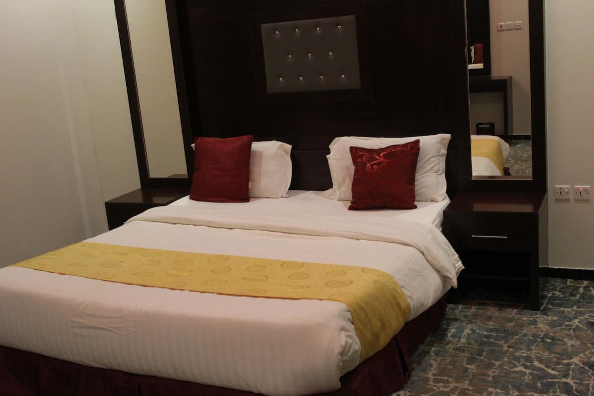 Een hotelkamer met een groot bed, twee nachtkastjes, een spiegel en een kamerbreed tapijt met dessin.