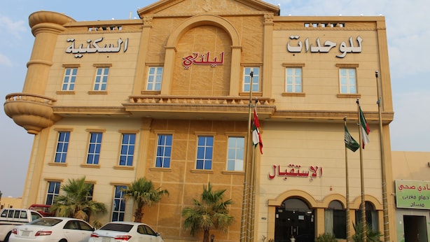 A large, beige building with multiple windows and a central entrance. There are flags on poles in front of the building. - Laylati Al Yarmouk (Riyadh)