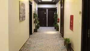 A hallway with a patterned floor, two doors at the end, and potted plants along the sides. - Laylati Al Yarmouk (Riyadh)