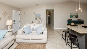 A modern living room with a white sofa, a kitchen island with stools, and a hallway leading to another room.
