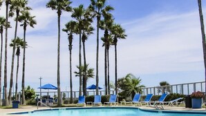 A swimming pool with blue lounge chairs and palm trees in the background. - WATER VIEW! POOL! HOT TUB! SAUNA! GYM! WALK TO BEACH! PET FRIENDLY! (Corpus Christi)