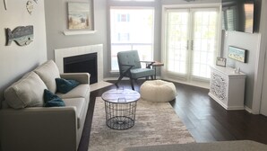 A living room with a fireplace, a sofa, a round coffee table, and a television. - WATER VIEW! POOL! HOT TUB! SAUNA! GYM! WALK TO BEACH! PET FRIENDLY! (Corpus Christi)