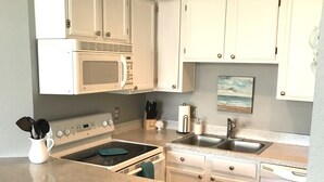 A kitchen with white cabinets, a microwave, stove, sink, and a small rug. - WATER VIEW! POOL! HOT TUB! SAUNA! GYM! WALK TO BEACH! PET FRIENDLY! (Corpus Christi)