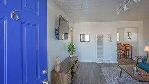 A living room with a blue door, a wooden console table, a potted plant, a sofa, a coffee table, and a dining area with a table and chairs. - Walk to UNM, 1bd/1ba, Clean! (Albuquerque)