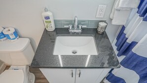 A bathroom with a white toilet, a sink with a speckled countertop, and a glass container with cotton balls. - Walk to UNM, 1bd/1ba, Clean! (Albuquerque)