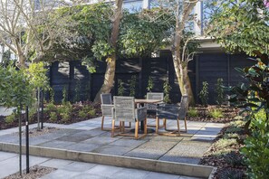 A patio area with a table and chairs, surrounded by trees and plants. - The Parque (Christchurch)