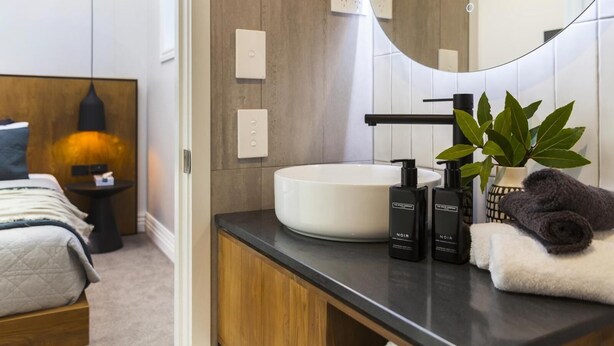 Un baño moderno con un espejo grande, un lavabo blanco y dos artículos de aseo negro.