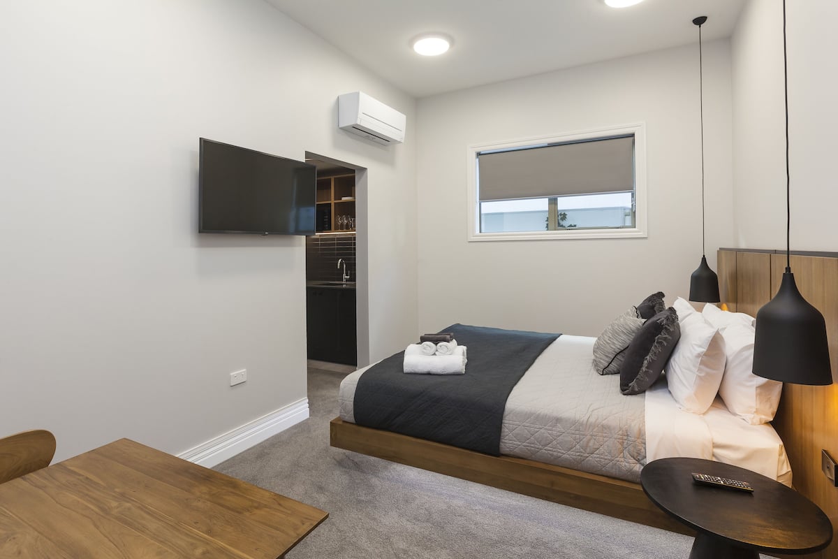 A bedroom with a bed, bedside table, and a TV mounted on the wall.