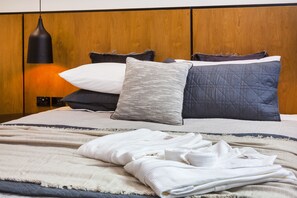 Una cama bien hecha con varias almohadas y una colcha, una lámpara de noche y un cabecero de madera.