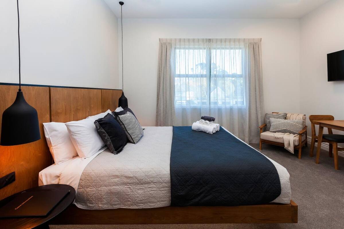 A hotel room with a large bed, a desk, a chair, a TV, and a window with curtains.