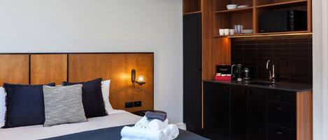 Habitació d'hotel amb un llit, una taula de nit amb una làmpada, un armari de fusta integrat amb electrodomèstics de cuina i una petita zona de seients.