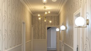 Un pasillo con papel tapiz estampado, una lámpara de araña moderna y apliques de pared.
