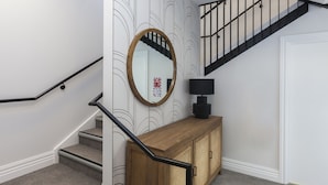 Una escalera con barandilla negra, una consola de madera con espejo y una pared con un diseño decorativo.