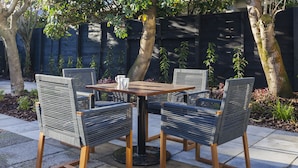 Un patio con una mesa redonda y cuatro sillas, rodeado de un jardín con árboles y plantas.