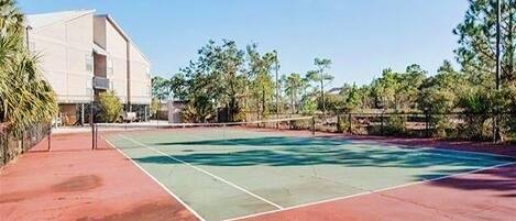 An outdoor tennis court with a building in the background.