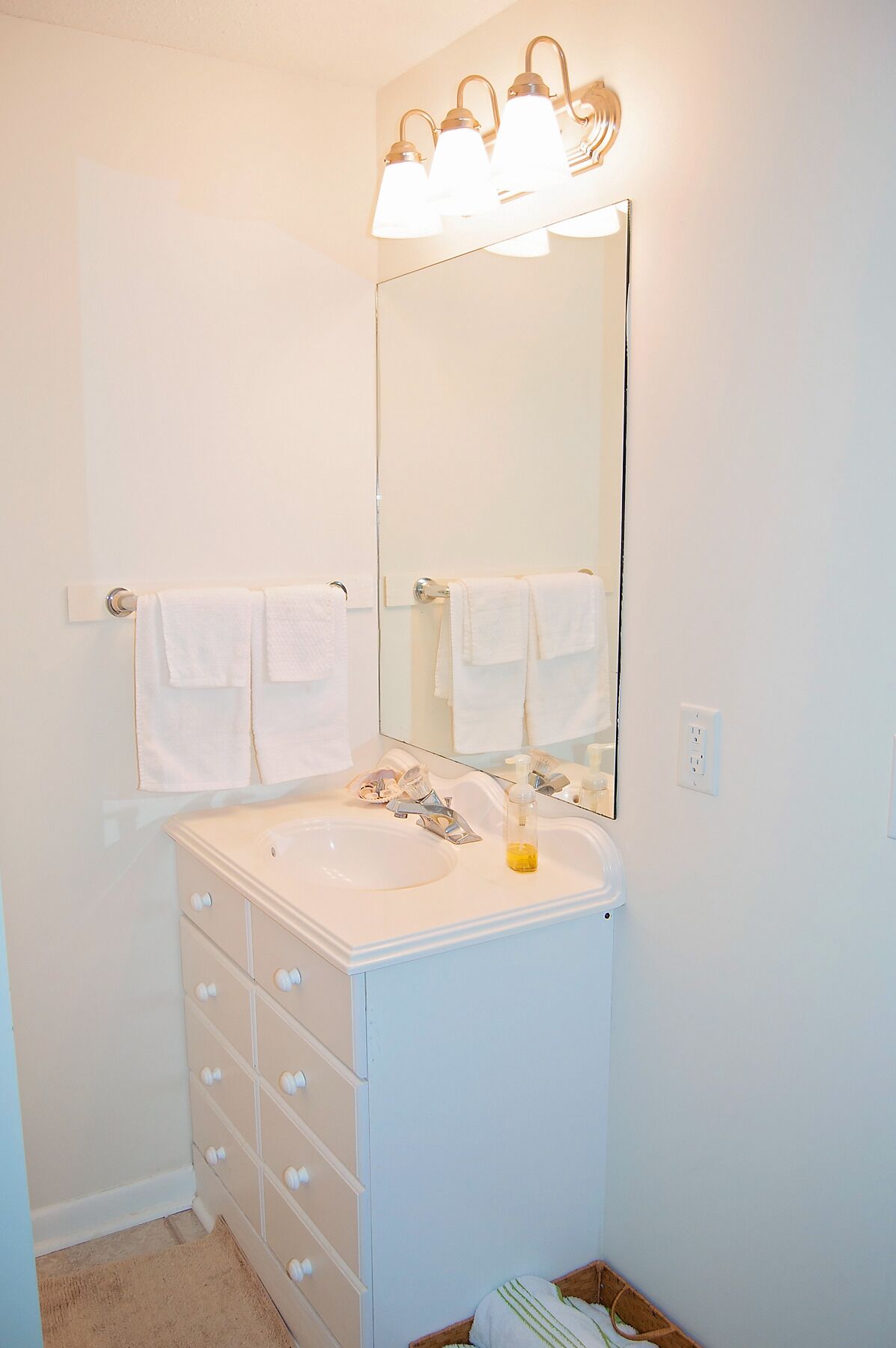 Une salle de bain avec un lavabo blanc, trois luminaires au-dessus du miroir et deux serviettes suspendues à des porte-serviettes.