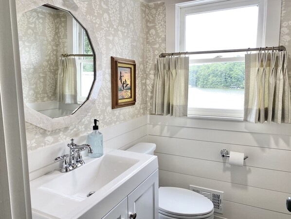 A bathroom with a white sink, a mirror, a toilet, and a window with curtains.