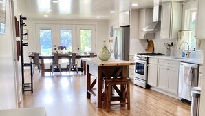 Une cuisine spacieuse avec un plancher en bois, un coin repas comprenant une table et des chaises, et une vue sur l’extérieur grâce à de grandes fenêtres.