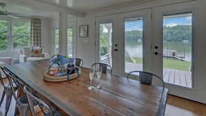 Un coin repas avec une table en bois, des chaises et une vue sur un lac, visible à travers de grandes portes coulissantes.