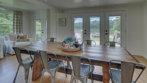 Un espace repas avec une grande table en bois, des chaises en métal et une vue sur un lac, visible à travers des portes vitrées.