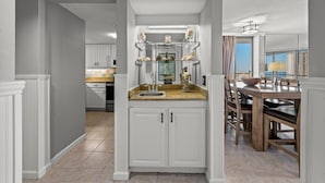 A modern kitchen with white cabinetry, a granite countertop, and a dining area with a wooden table and chairs.