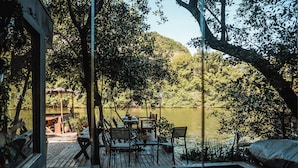 Una terraza de madera con mesas y sillas que da a un lago, rodeada de árboles.