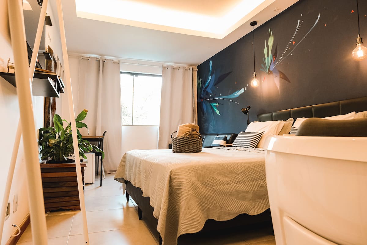 Un dormitorio con una cama, una mesita de noche, una lámpara, una planta y una pared con un mural floral.