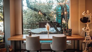 Una zona de estar acogedora con una mesa de madera, dos sillas y un ventanal con vistas a árboles y un edificio.