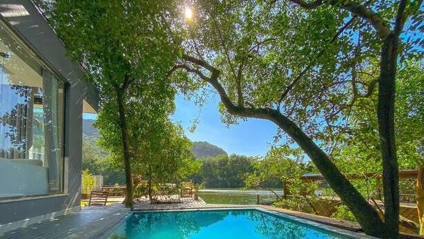 Una piscina con borde de baldosas, rodeada de árboles y vistas a un lago y montañas.
