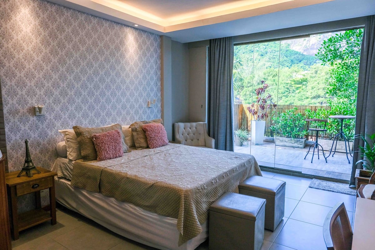 Un dormitorio con una cama grande, una mesita de noche, una silla y vistas a un balcón con plantas y una mesa.