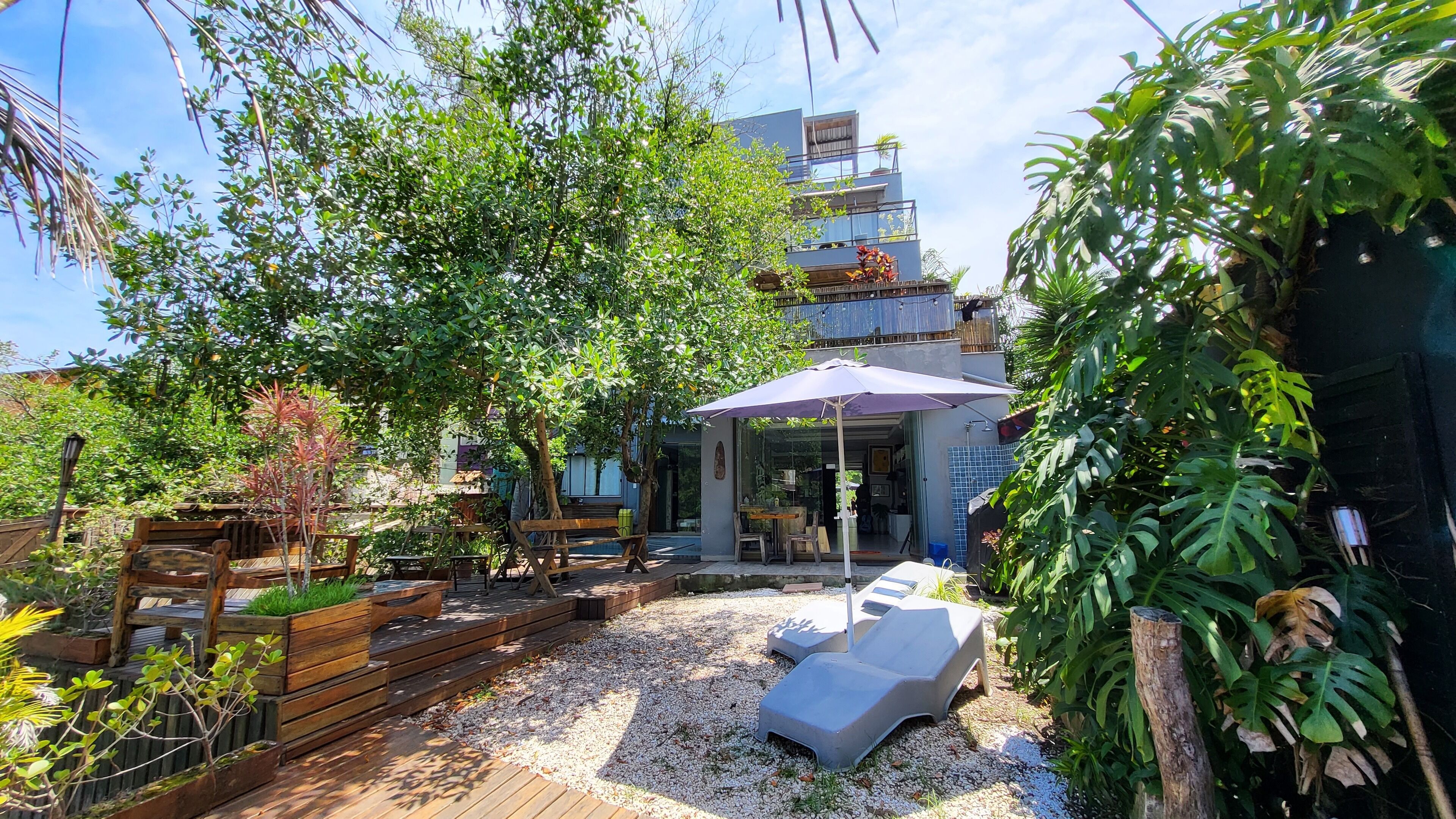 Un espace patio aménagé avec du mobilier en bois, un coin salon couvert et une vue sur un immeuble doté d’un balcon.