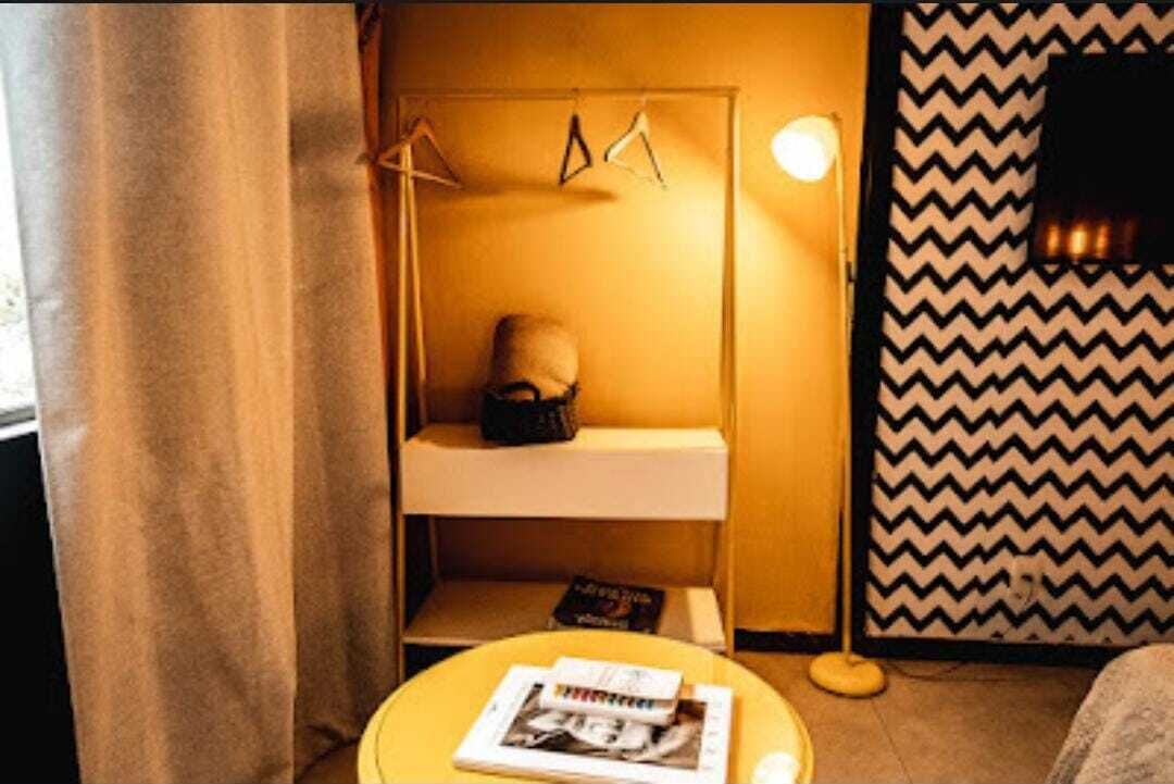 A compact hotel room with a bed, a small bedside table with a magazine, a hanging light, and a chevron-patterned wall.